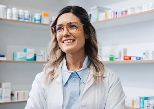 Woman in white coat smiling in the pharmacy. 