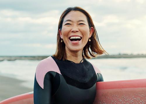 Woman smiling while holding surf board on the beach. 