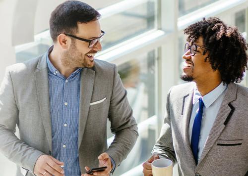 Two men in business attire smiling at each other. 